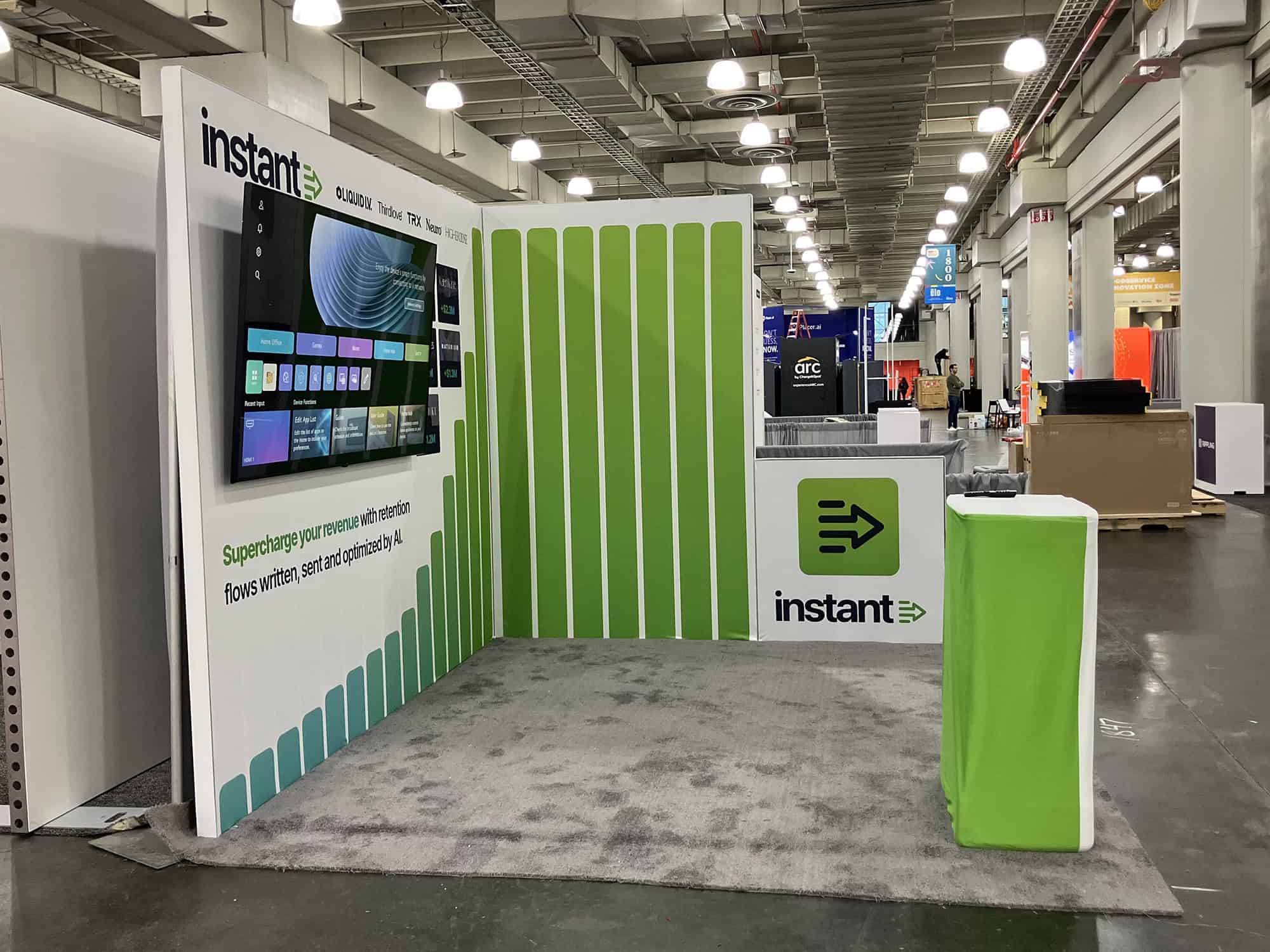 A vibrant trade show booth designed by Expo-at, featuring a large digital display wall, green and white branding elements, and a modern setup to attract visitors at conventions and exhibitions.